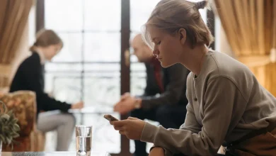 Teenager focused on a smartphone at home with adults blurred in the background